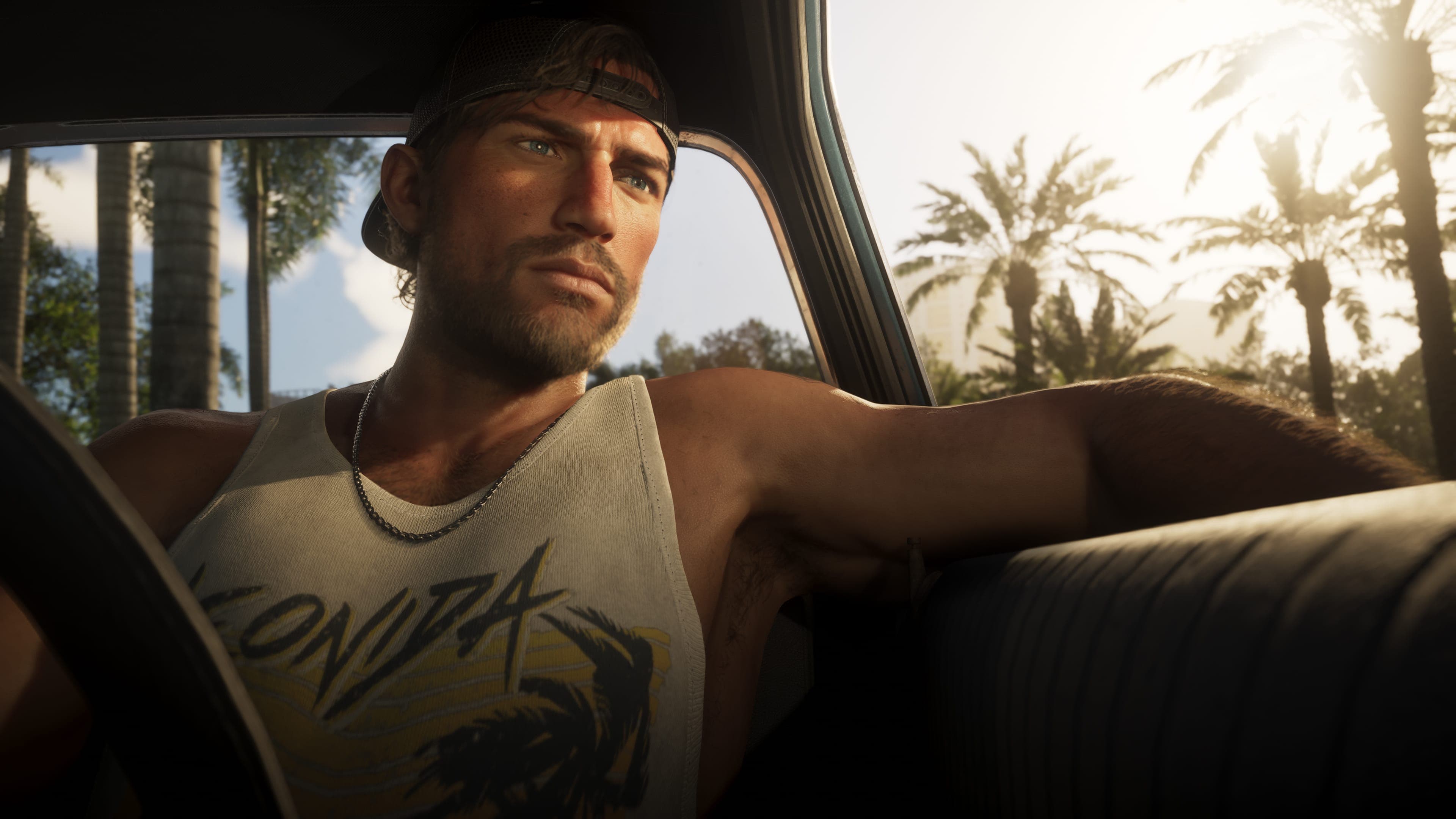Jason in the driver's seat of a car, in a backwards cap and a Leonida vest, one arm stretched along the seat back, palm trees in the sun beyond the window.