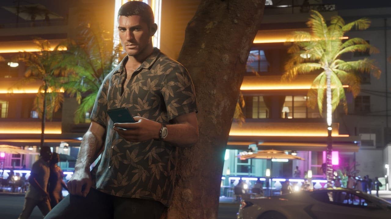 Jason leaning against a palm trunk on a neon-lit street at night, checking his phone.