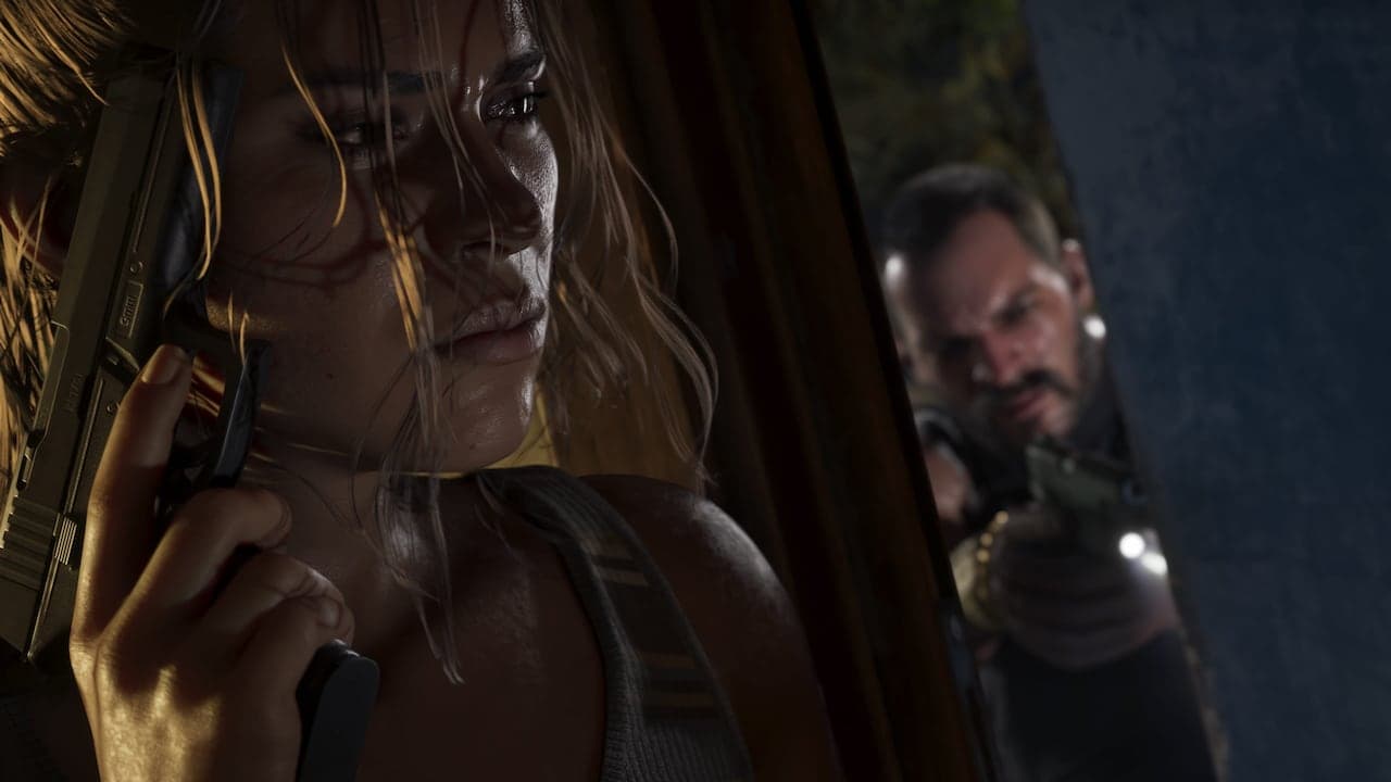 Lucia pressed against a wall in close-up holding a pistol upright, as an armed figure with a torch searches through the window behind her.