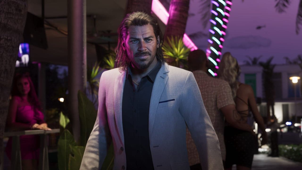 Raul walking a neon-lit street at night in a pale suit, bar tables and passers-by around him.
