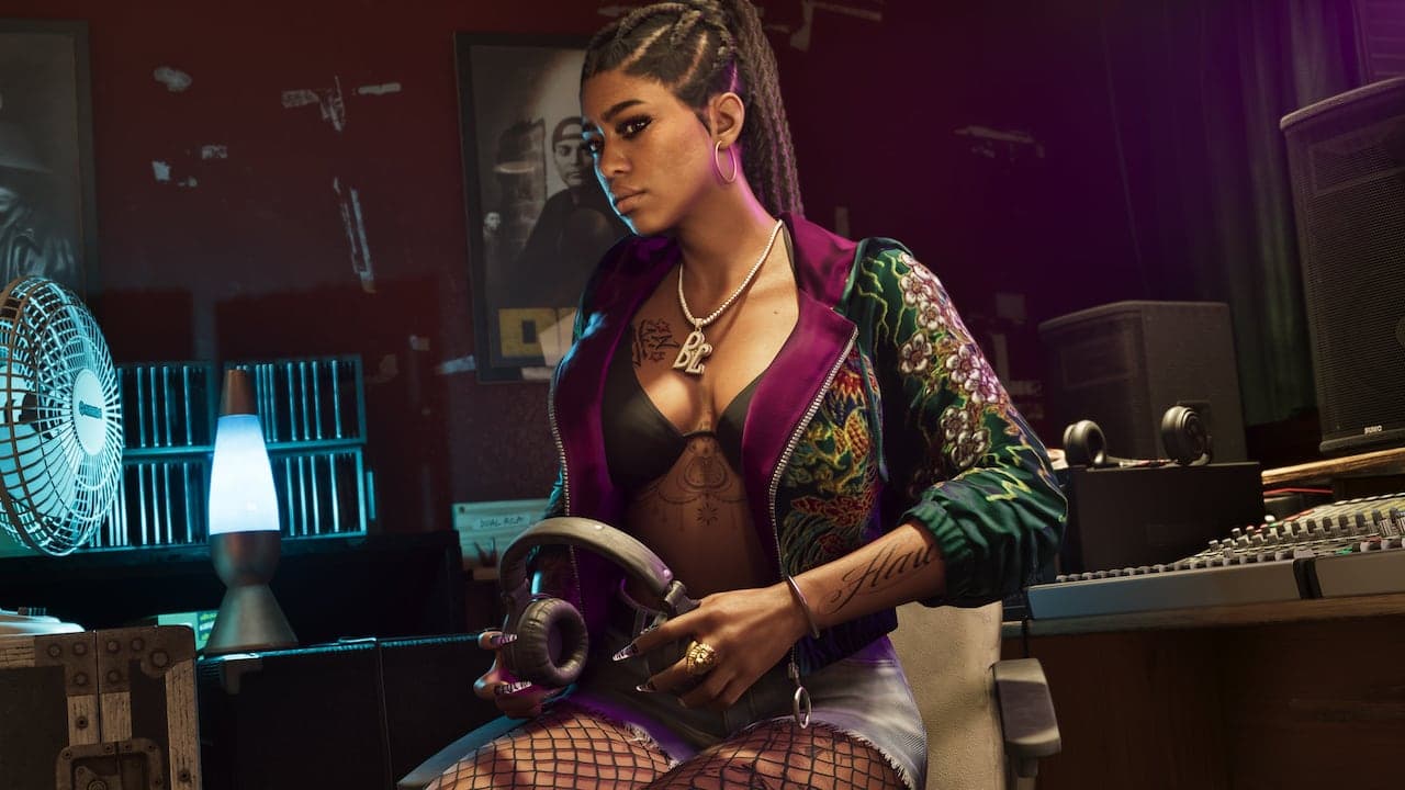 One of Real Dimez seated in a studio control room in an embroidered bomber jacket, headphones in her hand.
