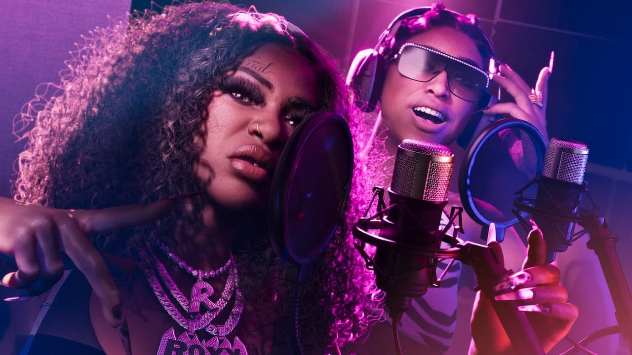 The two members of Real Dimez recording together at studio microphones under pink light.