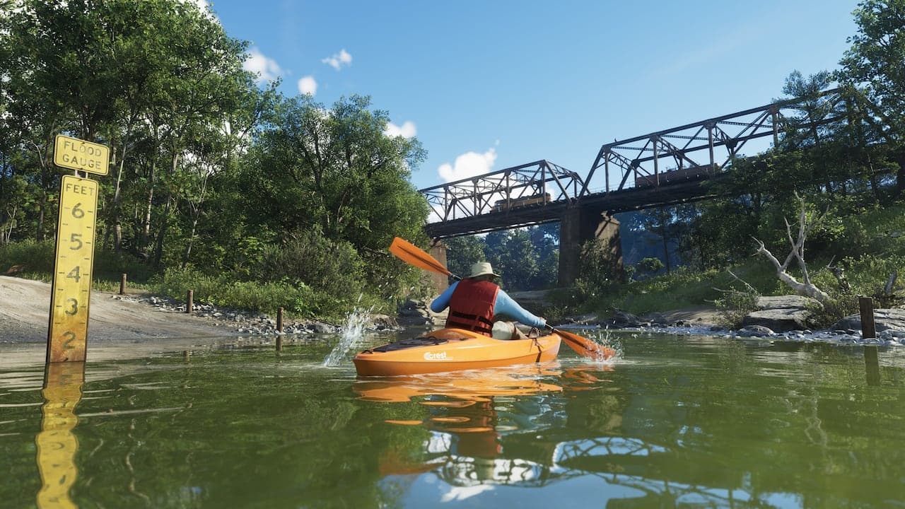 A kayaker paddling a green river in Mount Kalaga National Park beneath a steel railway trestle, a flood gauge staked at the water's edge.