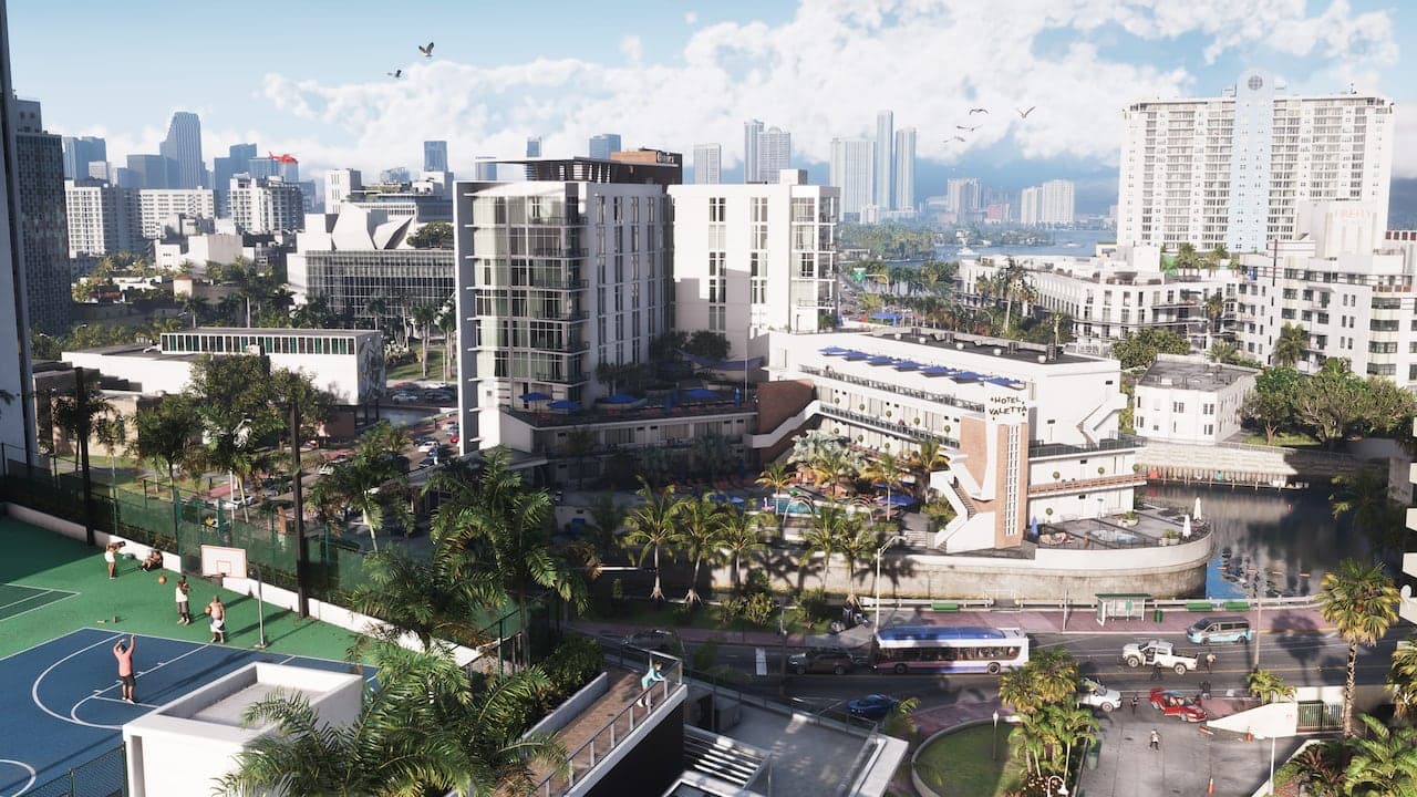 A daytime view across Vice City rooftops to the bay, hotel towers and a basketball court below, the downtown skyline on the horizon.