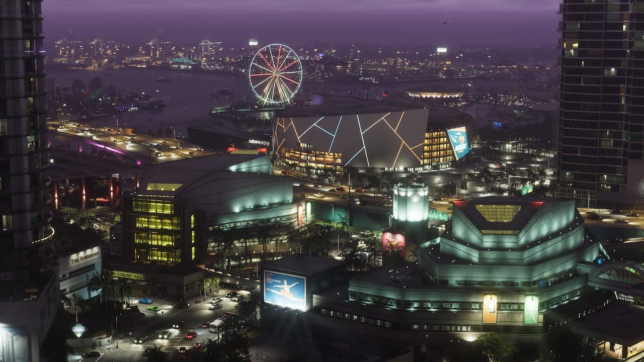 Vice City at night from above: an arena, a concert hall and a lit observation wheel on the waterfront, with the bay beyond.
