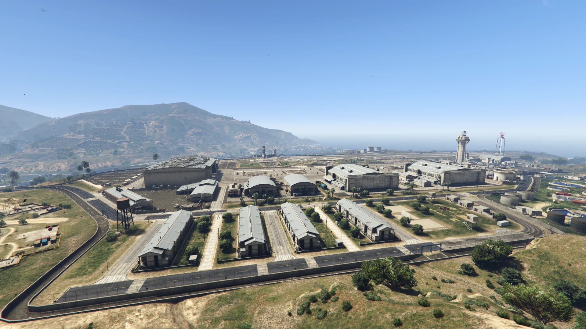 Fort Zancudo from the air, hangars and barracks laid out inside the perimeter with the mountains behind.