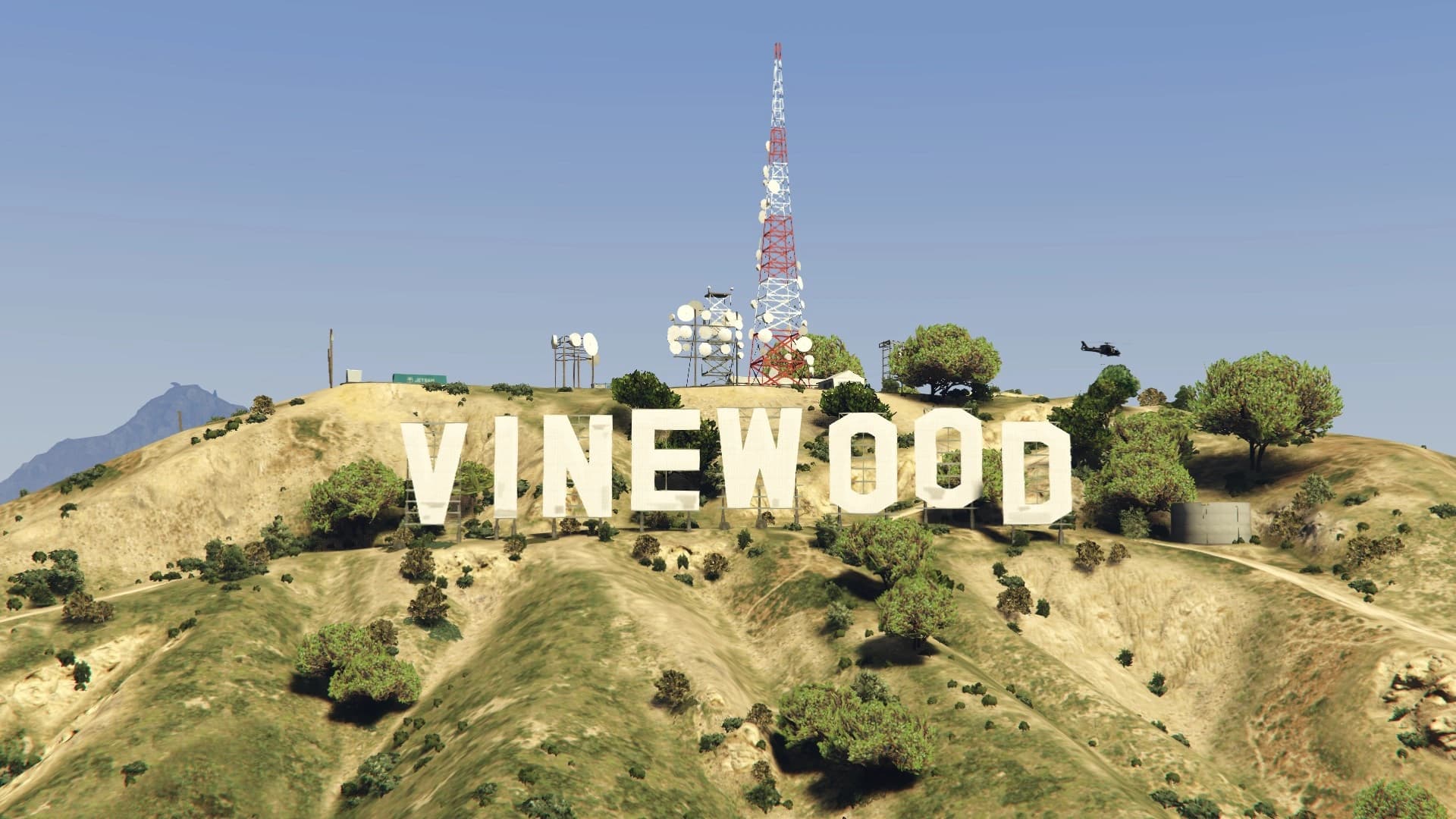 The Vinewood Sign along the ridge at sunset, its letters lit against a pink sky with the radio mast behind.