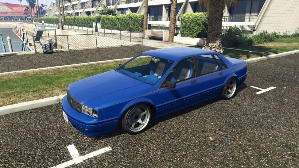 The Albany Primo Custom, a blue lowered 1990s four-door saloon, parked beside a lawn, in GTA Online.