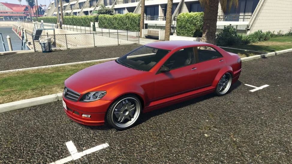 The Benefactor Schafter, a red four-door saloon, parked beside a lawn, in GTA Online.