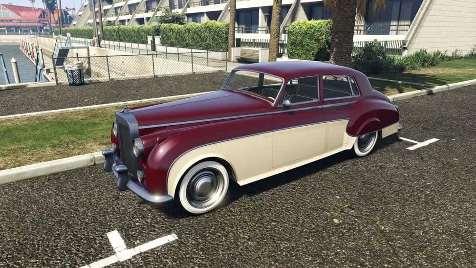 The Enus Stafford, a maroon and cream 1950s luxury saloon with whitewall tyres, parked beside a lawn, in GTA Online.