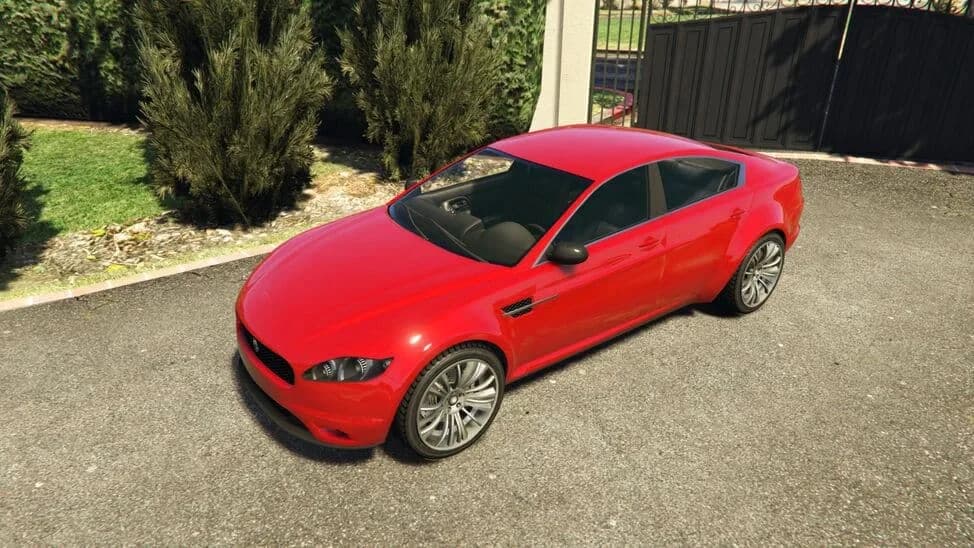 The Ocelot Jackal, a red four-door sports coupe, parked by a driveway, in GTA Online.