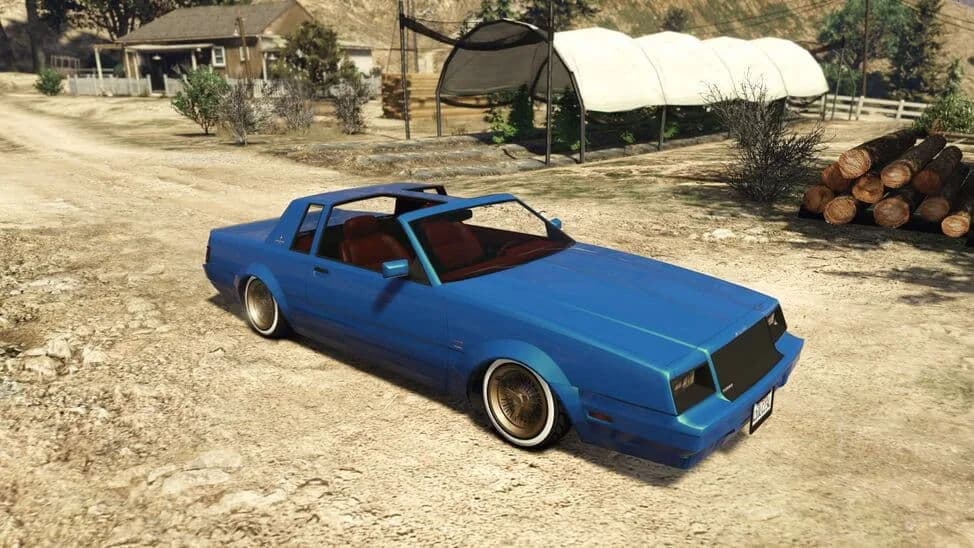 The Willard Faction Custom, a blue lowered 1980s coupe on wire wheels, parked on a dirt yard, in GTA Online.