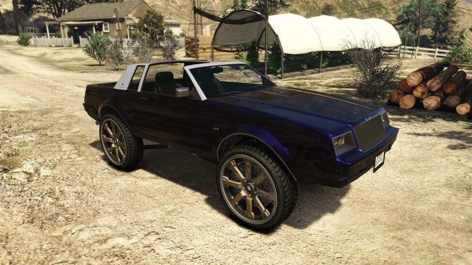 The Willard Faction Custom Donk, a dark 1980s coupe raised on huge bronze wheels, parked on a dirt yard, in GTA Online.