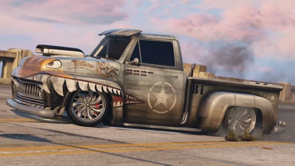 The Vapid Slamvan Custom, a slammed classic pickup in a shark-mouth livery with a blower, on a road, in GTA Online.