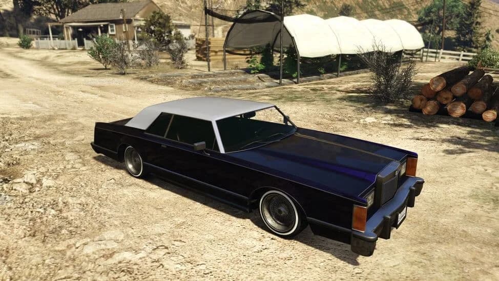 The Dundreary Virgo Classic Custom, a dark blue lowered 1970s luxury coupe with a white roof, parked on a dirt yard, in GTA Online.