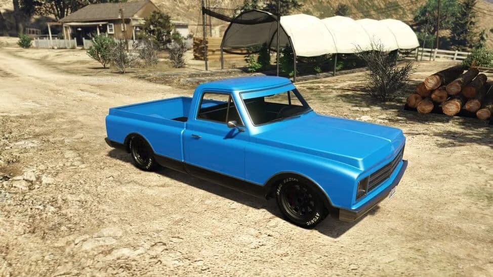 The Declasse Yosemite, a blue lowered late-1960s pickup, parked on a dirt yard, in GTA Online.