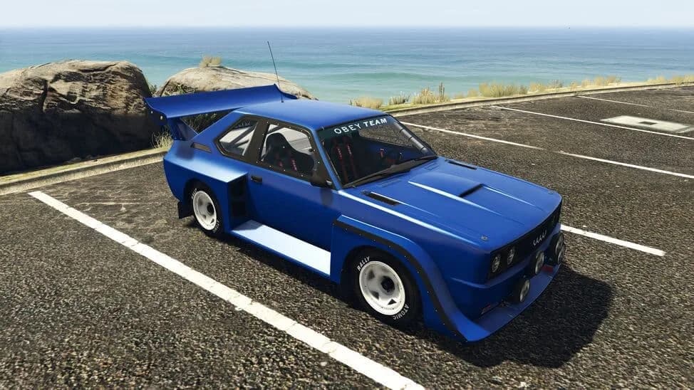 The Obey Omnis, a blue boxy rally car with wide arches and a rear wing, parked by the coast, in GTA Online.