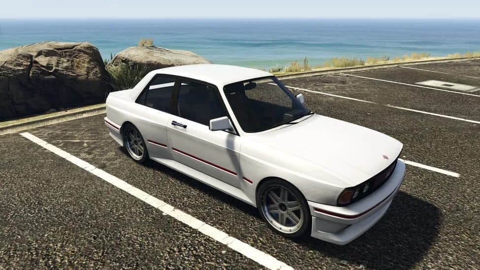The Übermacht Sentinel Classic, a white 1980s four-door sports saloon, parked by the coast, in GTA Online.