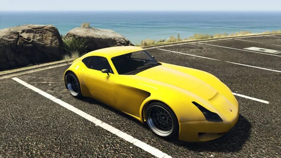 The Bravado Verlierer, a yellow front-engined sports coupe, parked by the coast, in GTA Online.