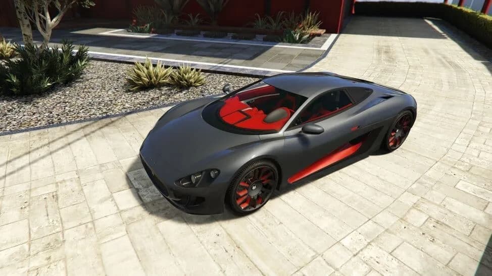 The Ocelot XA-21, a grey and red hybrid supercar, parked on a paved courtyard, in GTA Online.