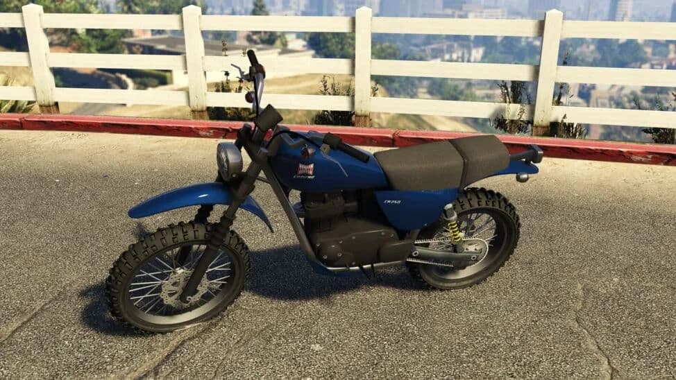 The Dinka Enduro, a blue trail motorcycle, parked by a white fence, in GTA Online.