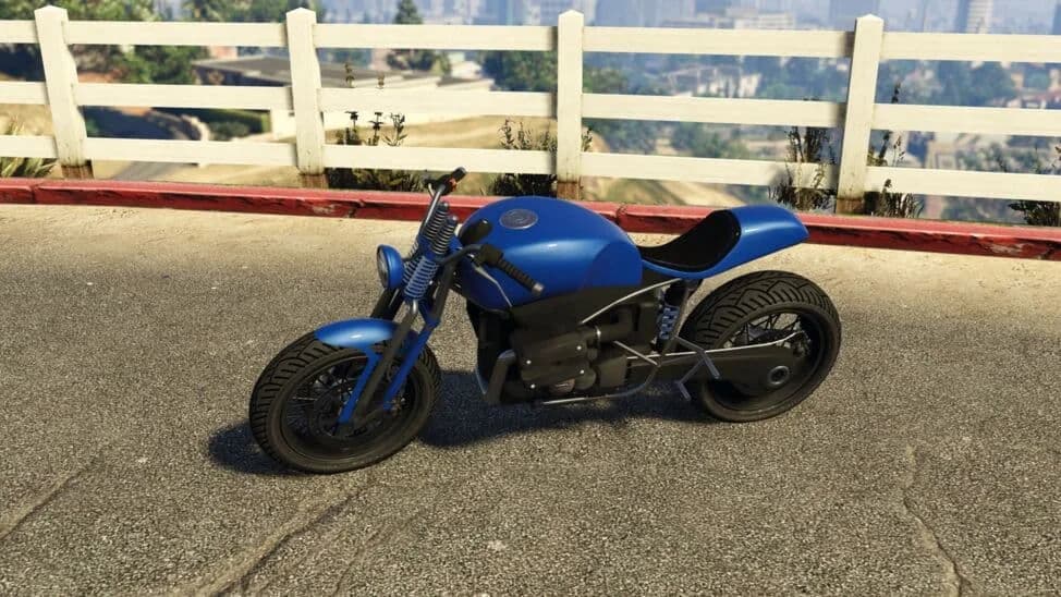 The Pegassi FCR 1000 Custom, a blue stripped café racer with a long seat, parked by a white fence, in GTA Online.