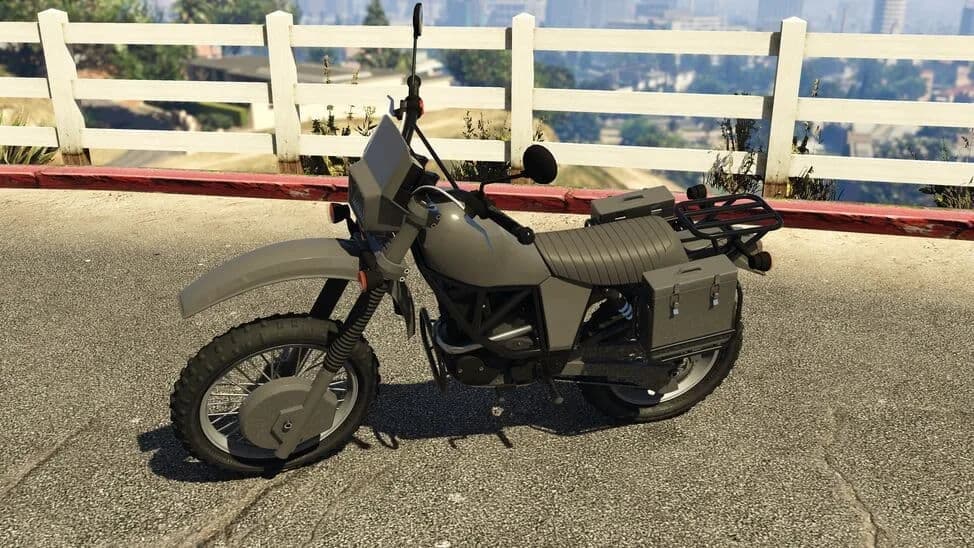 The Maibatsu Manchez Scout C, a grey armoured dual-sport motorcycle with side cases, parked by a white fence, in GTA Online.