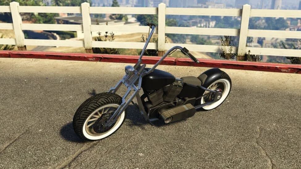 The Western Zombie Bobber, a black bobber motorcycle with whitewall tyres, parked by a white fence, in GTA Online.