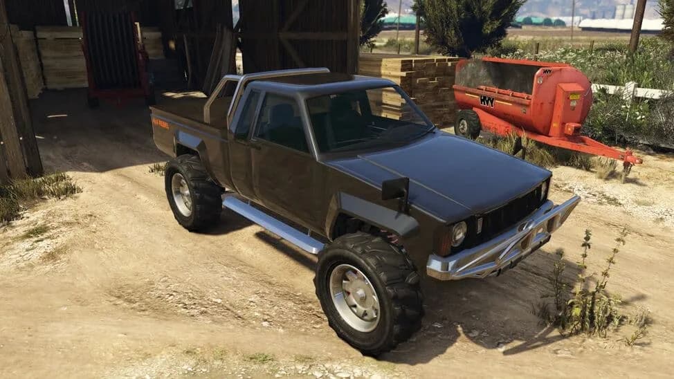 The Karin Rebel, a dark lifted compact pickup on off-road tyres, parked by a barn, in GTA Online.