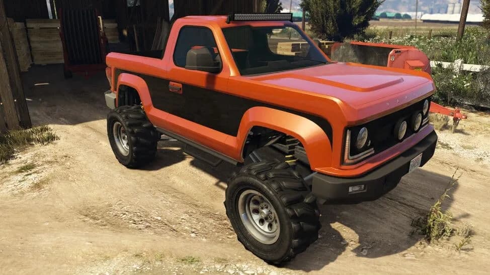 The Vapid Riata, an orange lifted pickup with a black side stripe and roof light bar, parked by a barn, in GTA Online.