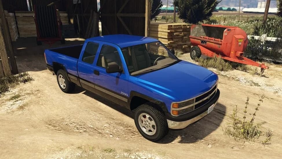 The Declasse Yosemite 1500, a blue 1990s extended-cab pickup, parked by a barn, in GTA Online.