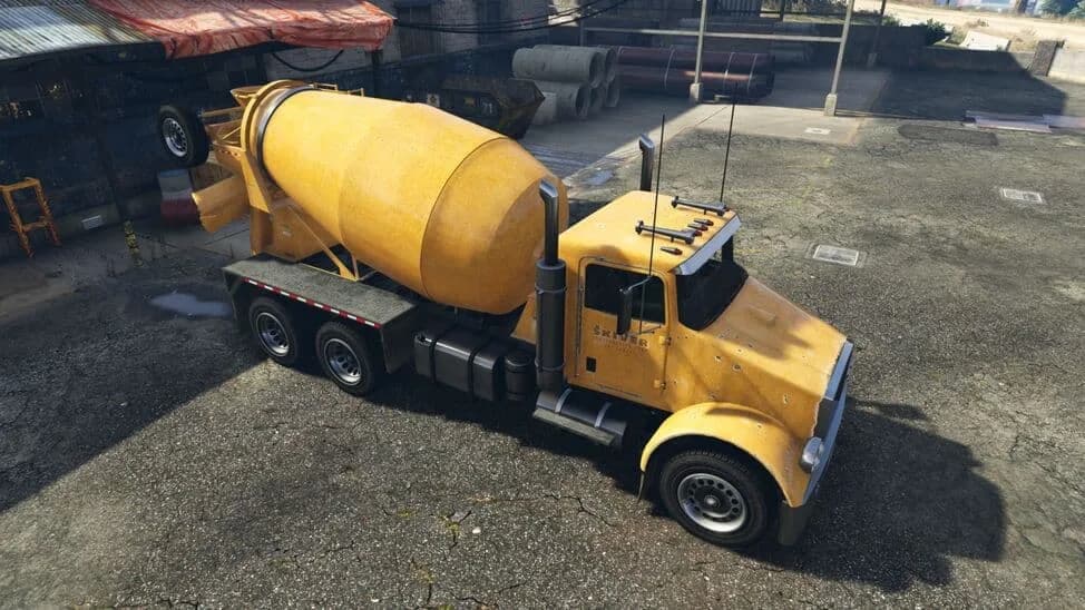 The HVY Mixer (4-Axle), a yellow long-nose cement mixer truck, parked in a builder's yard, in GTA Online.