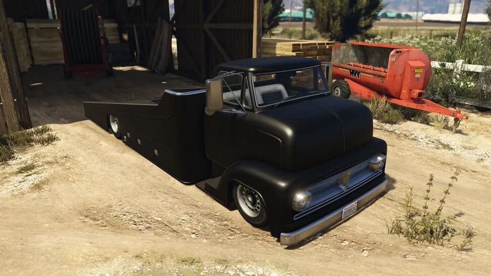 The Vapid Slamtruck, a black lowered 1950s-style flatbed truck, parked by a barn, in GTA Online.