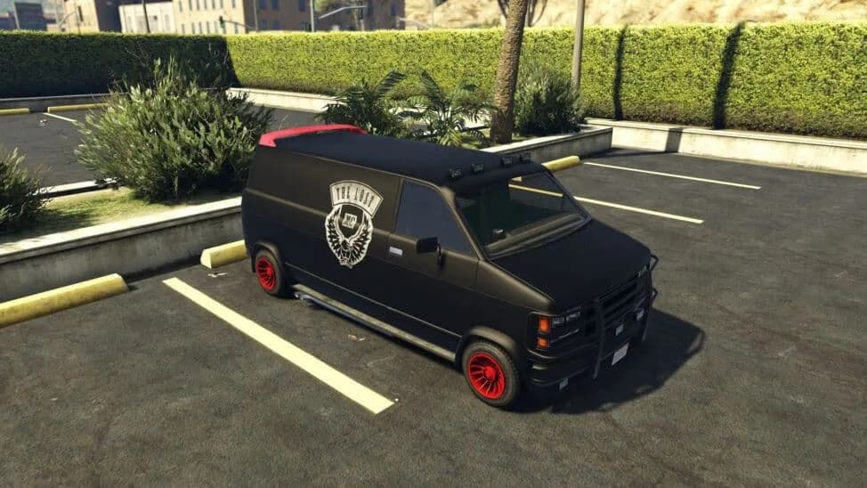 The Declasse Gang Burrito, a black van with a biker club's winged emblem, red wheels and a bull bar, parked in a car park, in GTA Online.