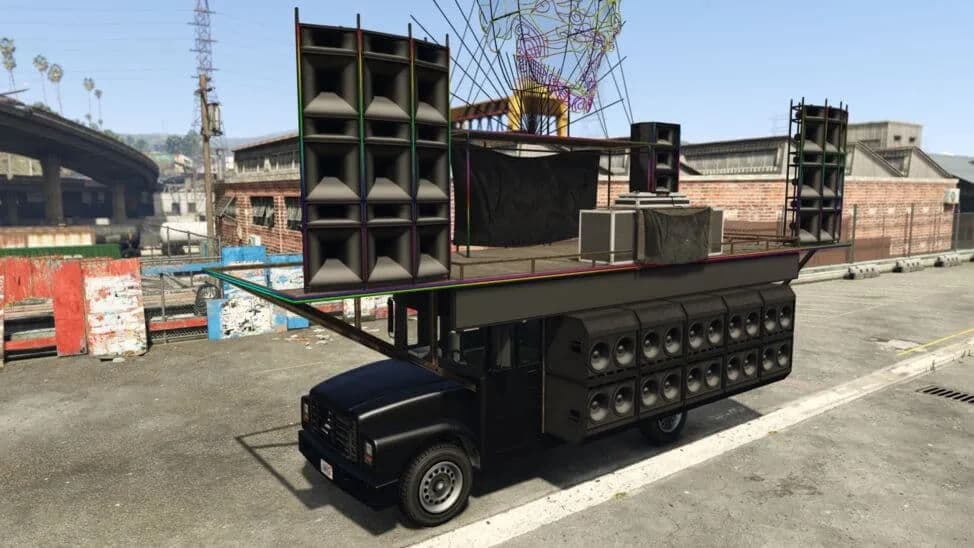 The Festival Bus, a black bus carrying a roof stage stacked with speakers, parked by a brick warehouse, in GTA Online.