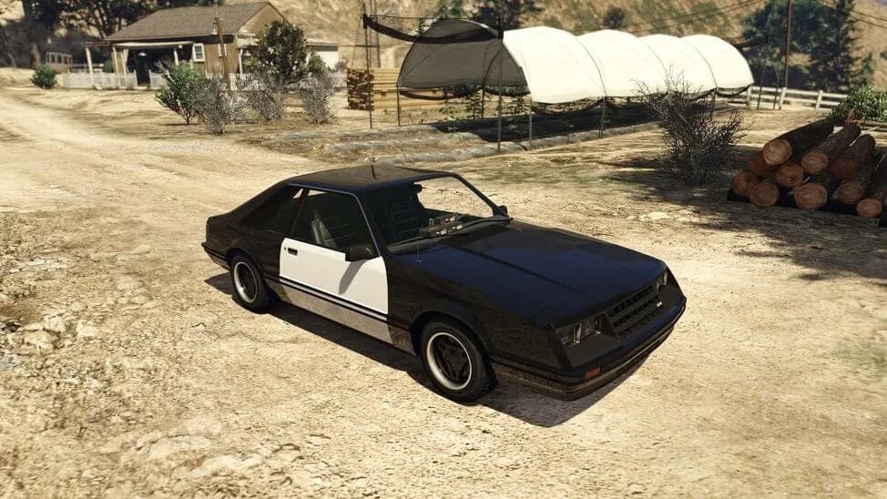 The Vapid Dominator FX Interceptor, a black and white early-1980s police muscle coupe, parked on a dirt yard, in GTA Online.