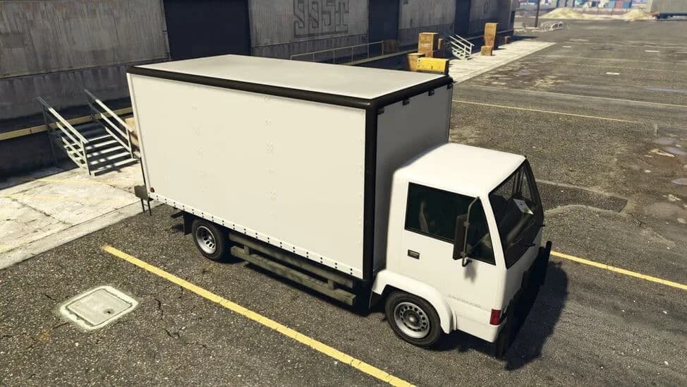 The Maibatsu Mule (Heist), a white box truck, parked by a warehouse, in GTA Online.