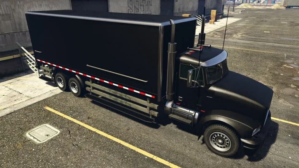 The MTL Pounder Custom, a black box-body lorry with chrome stacks, parked by a warehouse, in GTA Online.