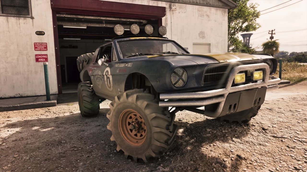 The ’67 Vapid Dominator Buggy, a dark muscle car raised on huge off-road tyres with a roof light bar and a racing number 6, parked outside an open garage door, in GTA VI.